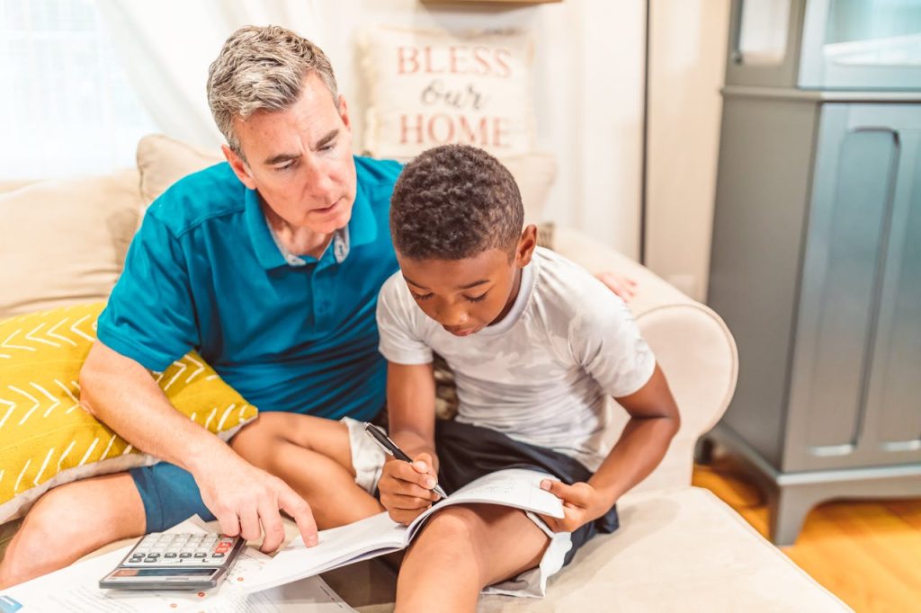 Father and son studying together at home, focused on homework with textbook and calculator.