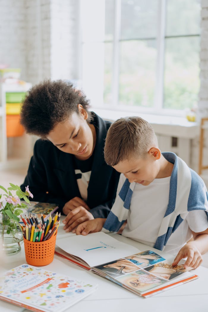 A teacher helps a student read a book in a bright classroom setting.