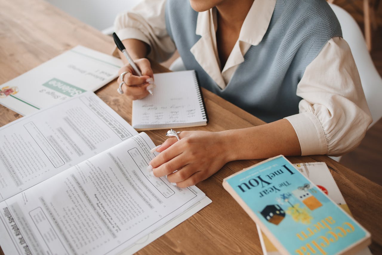 A person studying at a desk with books and a notepad, focusing on handwritten notes.