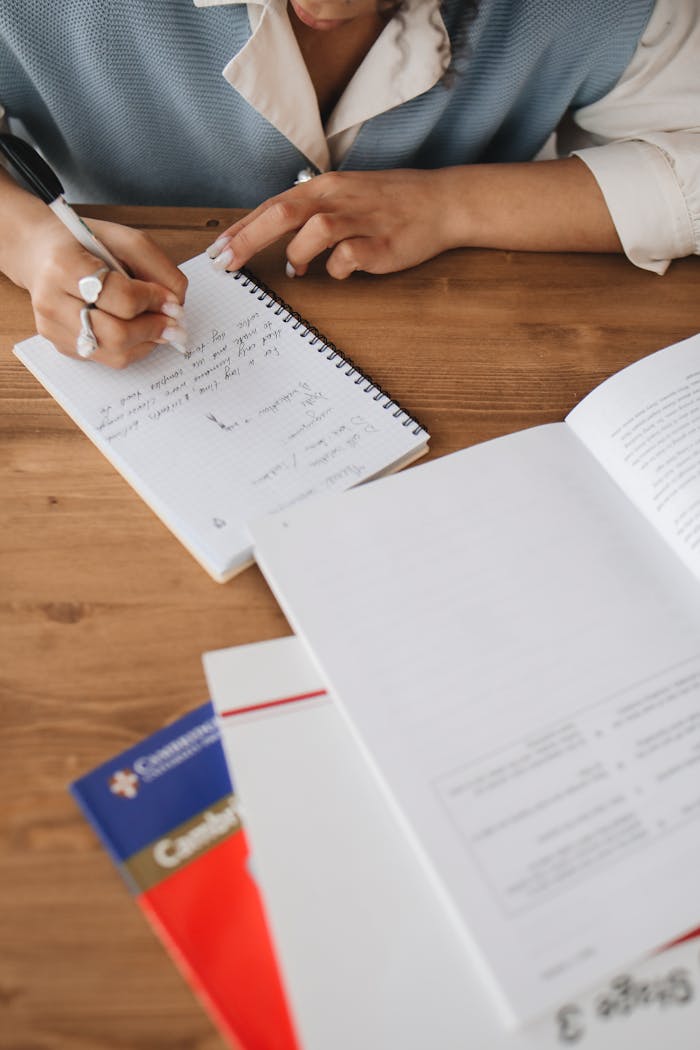 Close-up of a student writing in a notebook, studying at a wooden desk.