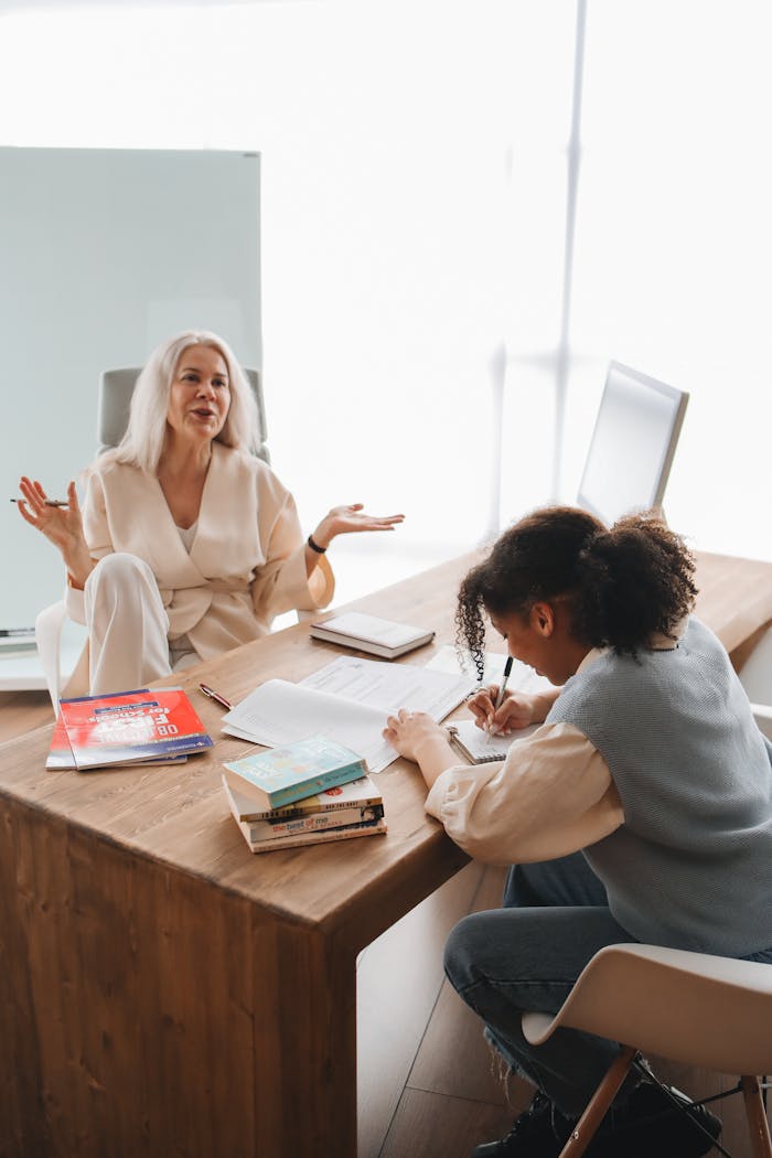 A teacher engages in a discussion with a student, with books and notes on the table.